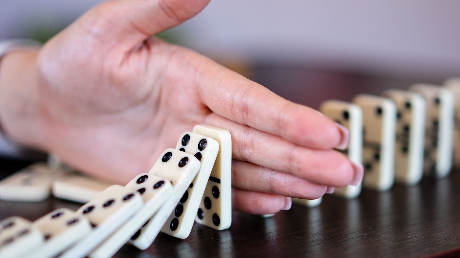 Een hand onderbreekt een rij vallende dominostenen